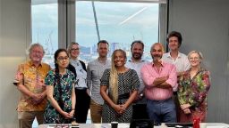 All members of the workshop stood for a photo in front of a window and behind the conference table